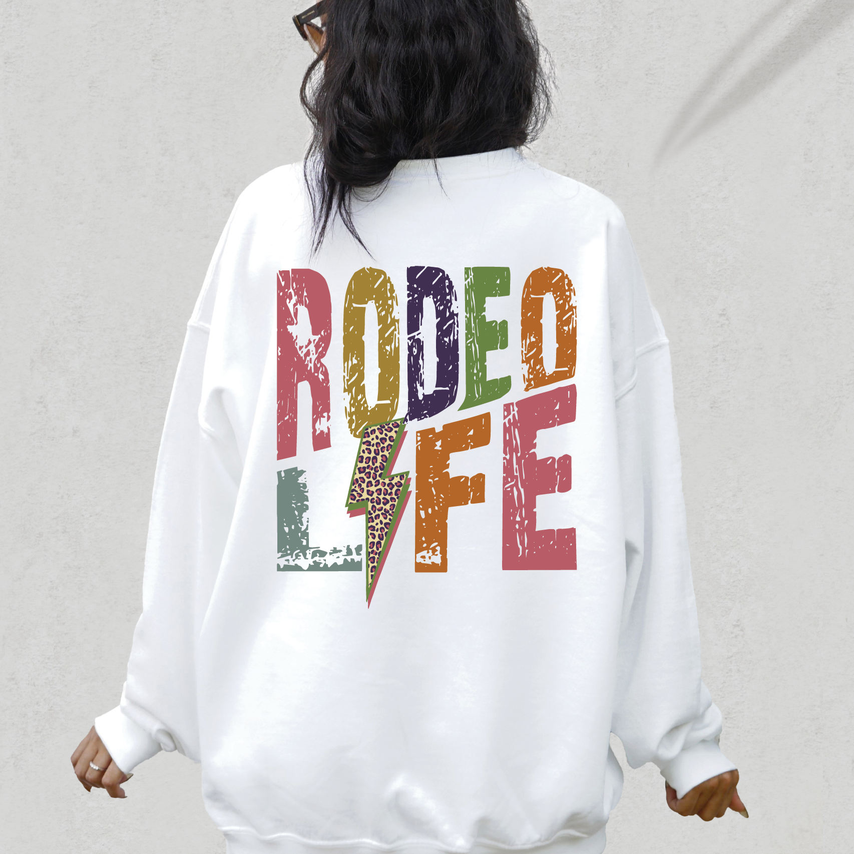 a woman wearing a white sweatshirt with the word rodeo life printed on it