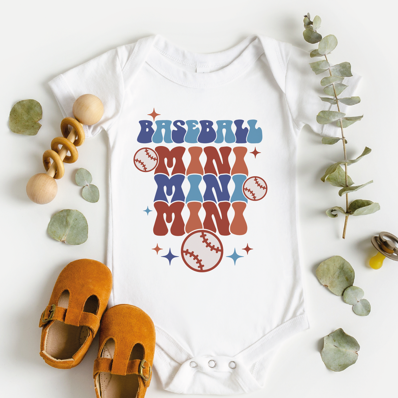 a baby bodysuit with a baseball mom runs on it next to a pair of